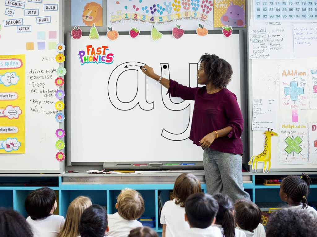 A teacher showing a group of young students how to write the letters ay on a smartboard